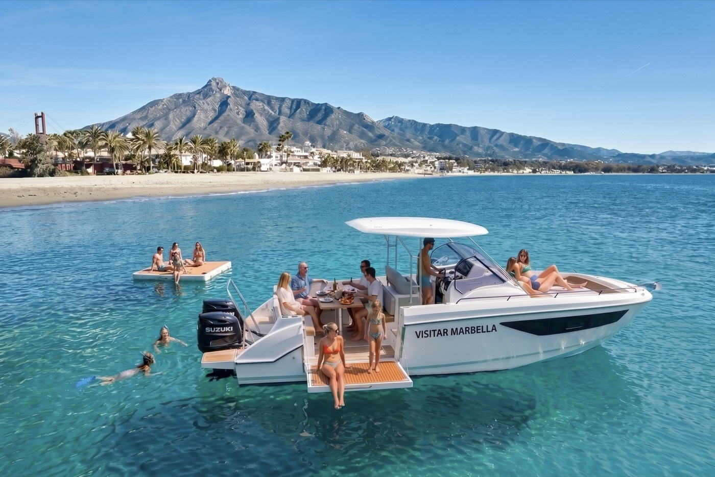 The Visitar Marbella boat at anchor off the Marbella coast with guests aboard and swimmers in the water, La Concha mountain behind