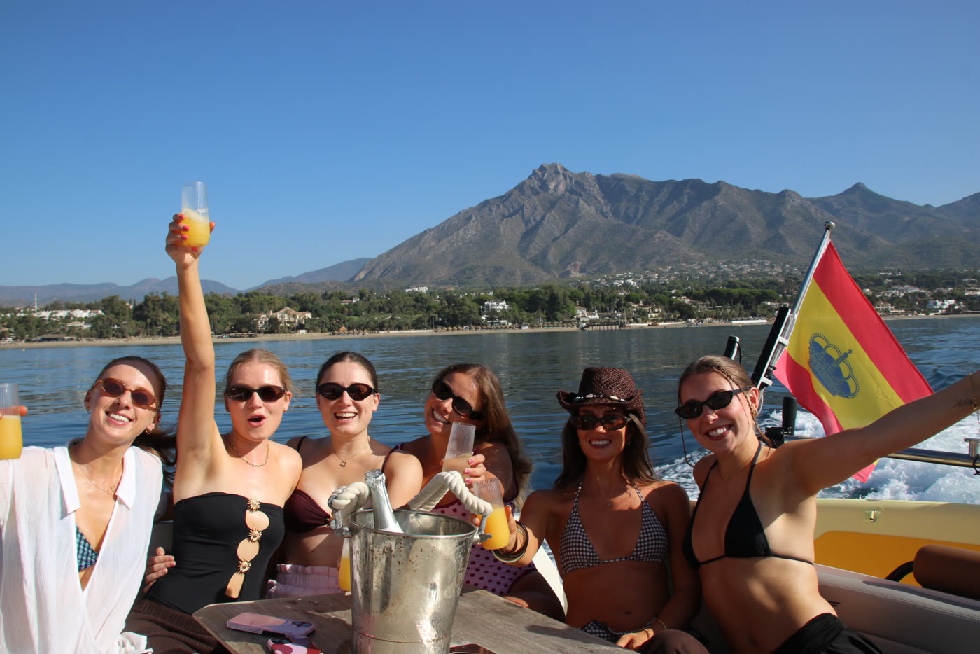 A group raising their drinks around the table on board, La Concha and the Marbella coast behind