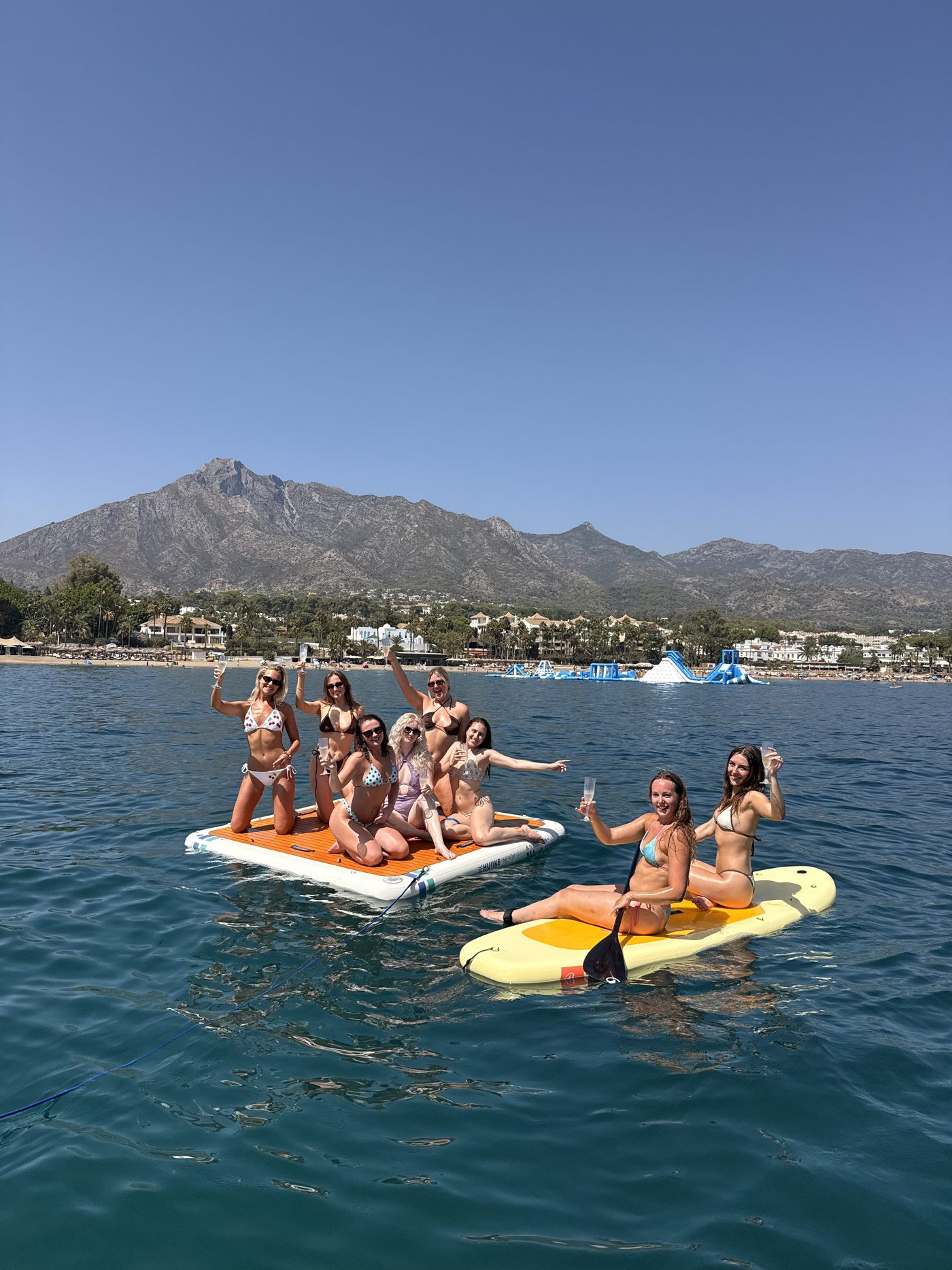 A group of friends together on the paddleboard beside the boat, the Marbella coastline and La Concha behind