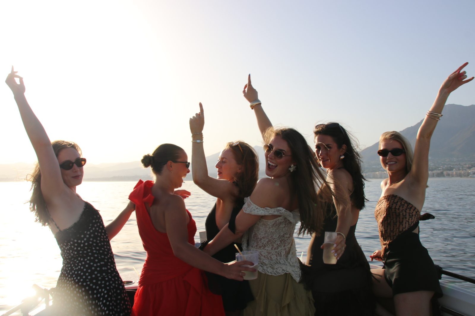 A group of friends dancing on the bow of the Visitar Marbella boat at golden hour, La Concha behind