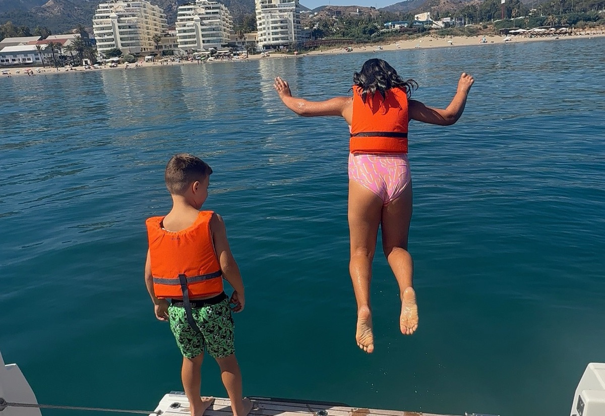 Kids in life vests jumping into the sea from the Visitar Marbella boat near the beach